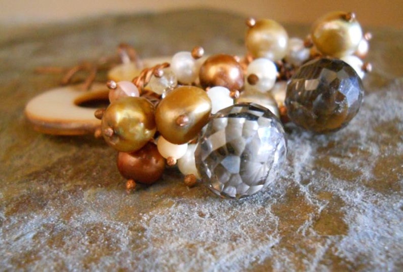 May include: A close-up of a bracelet with a mix of beads in various colors, including gold, bronze, white, and a faceted gray crystal. The bracelet is set against a textured background.