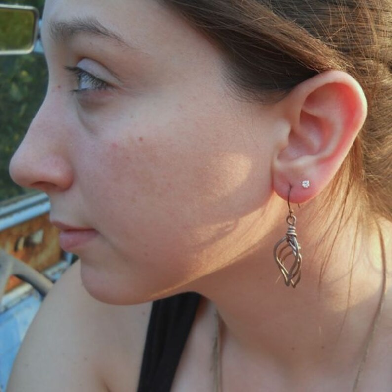 May include: A close-up of a person's ear with a small silver stud earring and a dangling silver earring with a geometric design.