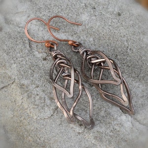 May include: A pair of copper wire earrings with a leaf design. The earrings are made of multiple layers of wire that are twisted and woven together.