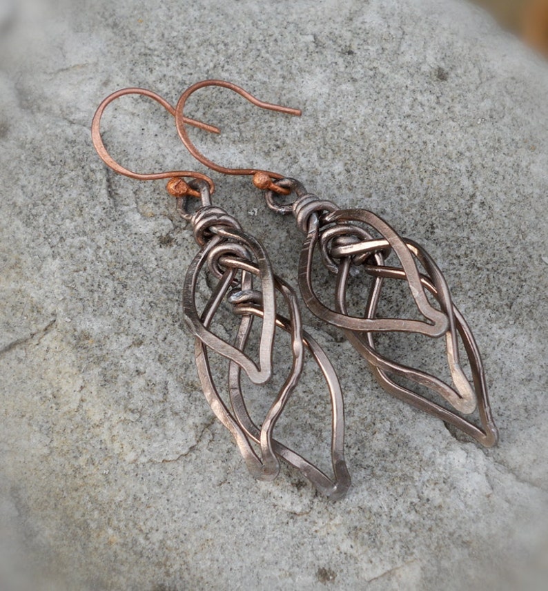 May include: A pair of copper wire earrings with a leaf design. The earrings are made of multiple layers of wire that are twisted and woven together.