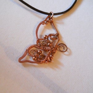 May include: Copper wire pendant with a butterfly design. The pendant features intricate wire wrapping and small copper beads. It hangs from a black leather cord, creating a unique and artistic necklace.