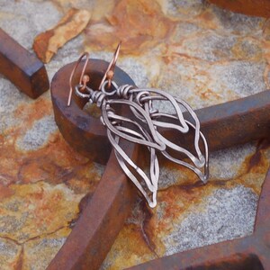 May include: A pair of silver dangle earrings with a delicate, leaf-like design. The earrings are made of wire and have a copper hook.