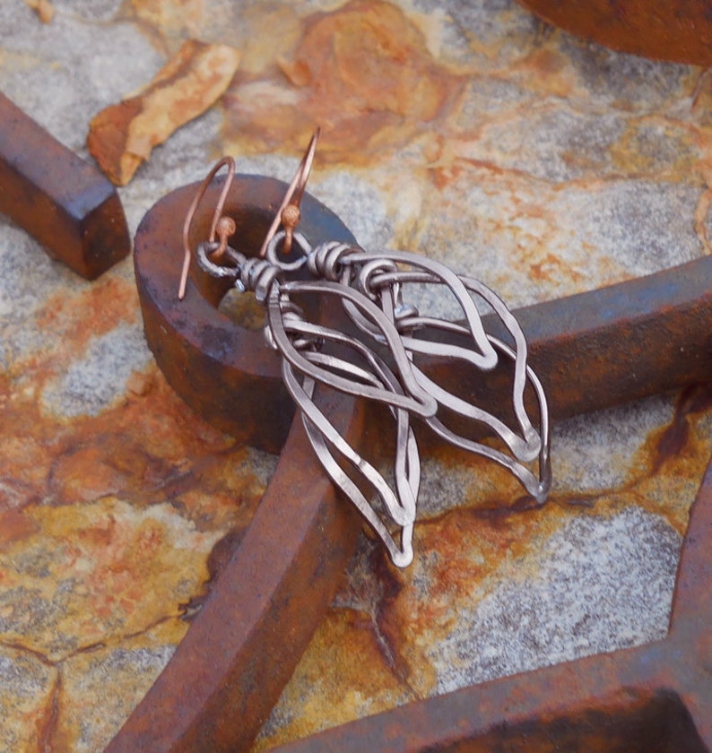 May include: A pair of silver dangle earrings with a delicate, leaf-like design. The earrings are made of wire and have a copper hook.