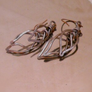 May include: A pair of silver-toned metal earrings shaped like leaves. The earrings are made of multiple layers of wire that are twisted and intertwined to create a delicate and intricate design.