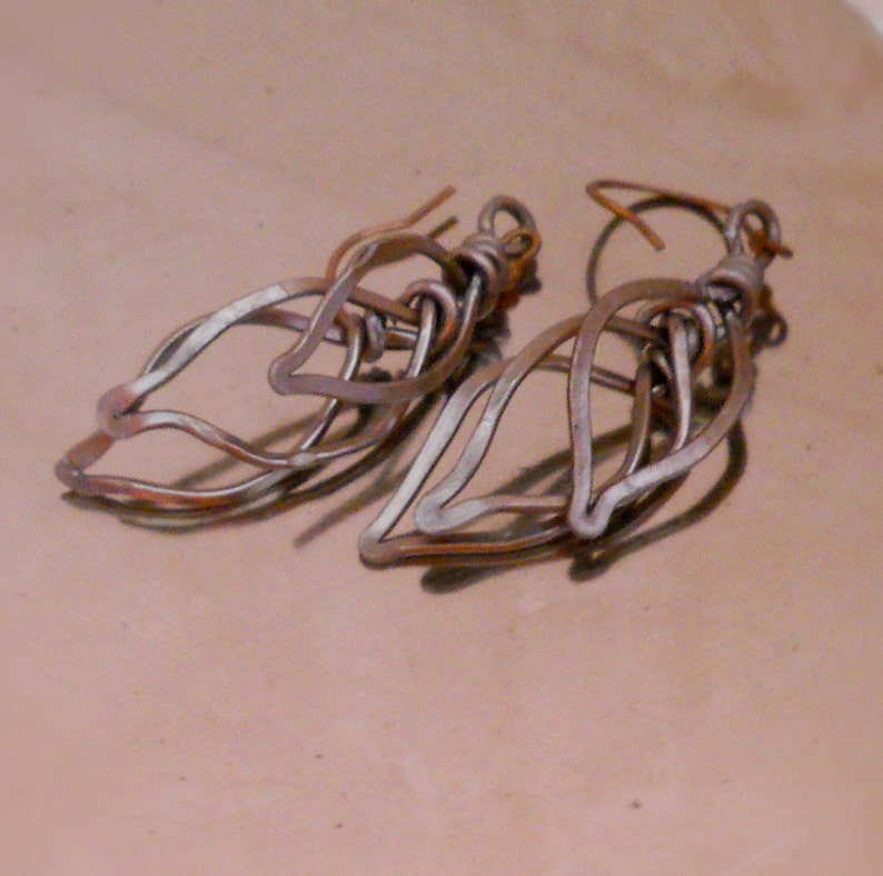 May include: A pair of silver-toned metal earrings shaped like leaves. The earrings are made of multiple layers of wire that are twisted and intertwined to create a delicate and intricate design.
