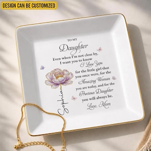 Könnte beinhalten: Eine quadratische weiße Keramikschale mit Goldrand, verziert mit einer violetten Blumenillustration und dem Text: To My Daughter, Even when I'm not close by, I want you to know I Love You for the little girl that you once were, for the Amazing Woman you are today, and for the Precious Daughter you will always be. Love, Mom. Der Name Sophia ist vertikal aufgedruckt.