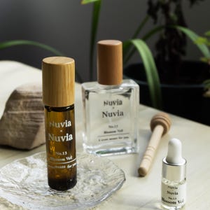 May include: Three glass bottles of perfume with wooden caps. The bottles are labeled "Nuvia x Nuvia" and "No. 13 Blossom Veil".