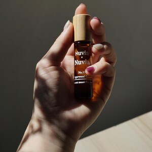 May include: A brown glass roller bottle with a bamboo lid. The bottle is labelled "Nuvia x Nuvia No.11 Agarwood Collection Scent meant for you".