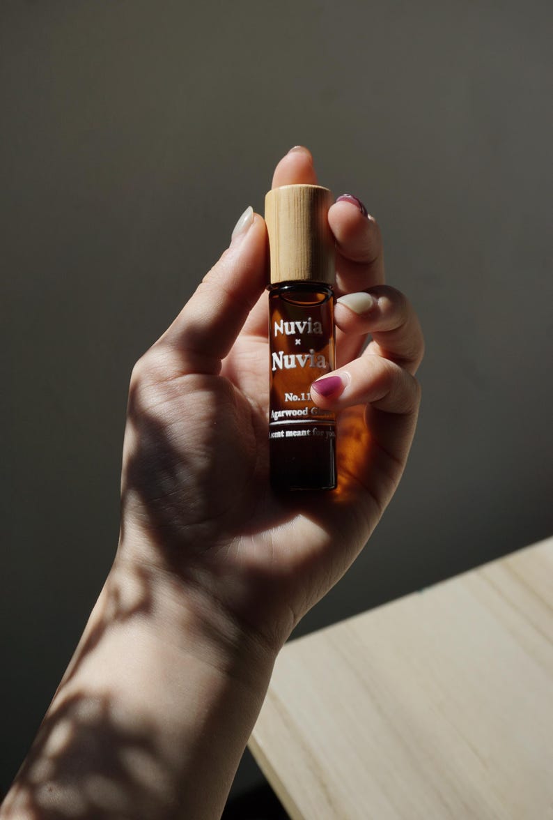 May include: A brown glass roller bottle with a bamboo lid. The bottle is labelled "Nuvia x Nuvia No.11 Agarwood Collection Scent meant for you".