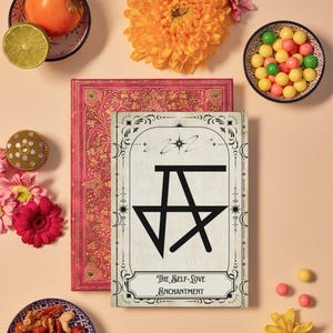 May include: A white card with a black star and the text "The Self-Love Enchantment" surrounded by a decorative border. The card is on top of a red book with a floral pattern. The image also includes a bowl of nuts, a bowl of colorful candies, a persimmon, a lime, and several flowers.