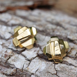 May include: A pair of gold geometric earrings with a textured finish. The earrings are made of multiple layers of metal that create a unique and modern design.