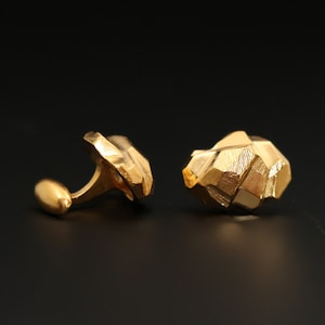 May include: A pair of gold cufflinks with a geometric, faceted design. The cufflinks are made of a shiny, polished metal.