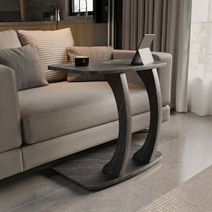 May include: A C-shaped side table with a black marble-patterned finish, featuring a flat rectangular base, two curved vertical supports, and a flat tabletop surface holding a small dark mug and a thin silver laptop computer.