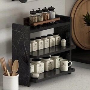 May include: A three-tiered black marble-patterned spice rack holding various glass spice jars on the top shelf and white ceramic canisters labeled with text like Tea, Sugar, and Coffee on the lower shelves, with a white utensil holder nearby.