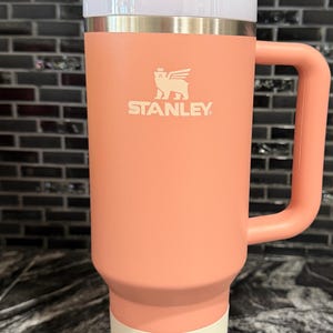 May include: A coral-coloured Stanley Quencher H2.0 Flowstate tumbler with a handle and a white lid. The tumbler has a straw and the Stanley logo. The tumbler is 1.18L and is designed for all-day hydration.
