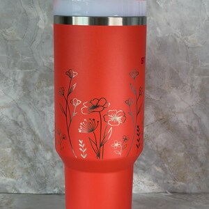 May include: A bright red insulated tumbler with a white lid and a silver rim. The tumbler has a floral design in silver and black. A white straw is inserted into the lid. The tumbler is designed to keep drinks cold or hot.