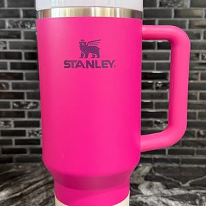May include: A vibrant pink Stanley Quencher H2.0 tumbler with a white lid and handle. The tumbler features a straw and the Stanley logo. The label indicates a capacity of 1.18 litres.