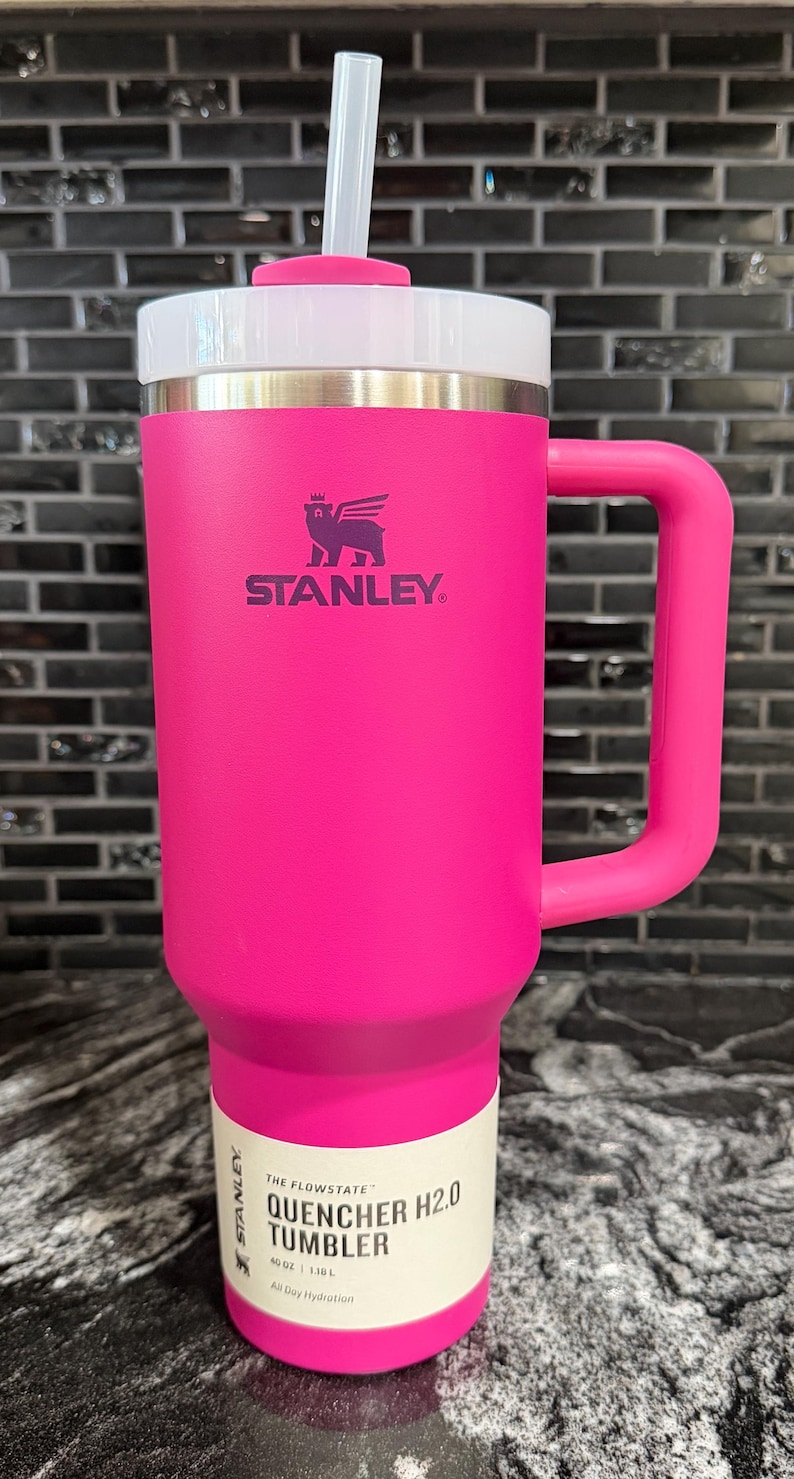 May include: A vibrant pink Stanley Quencher H2.0 tumbler with a white lid and handle. The tumbler features a straw and the Stanley logo. The label indicates a capacity of 1.18 litres.