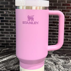 May include: A pink Stanley Quencher H2.0 Tumbler with a handle, lid, and straw. The tumbler features the Stanley logo and the text "THE FLOWSTATE QUENCHER H2.0 TUMBLER" on the label. It holds 1.18 litres.
