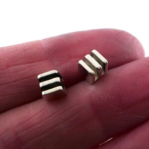 May include: A pair of silver cufflinks with a geometric design. Each cufflink is a small cube with three horizontal lines.