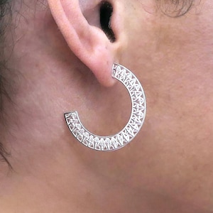 May include: Silver hoop earrings with a geometric design. The earrings are made of a delicate, intricate pattern of triangles.