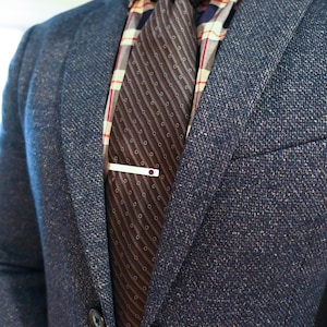 May include: A brown and white patterned tie with a silver tie bar with a purple stone. The tie is worn with a blue blazer.