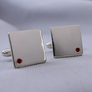 May include: A pair of silver cufflinks with a small red gemstone on each.