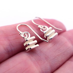 May include: A pair of silver dangle earrings with a geometric design. Each earring features a stack of four rectangular shapes.