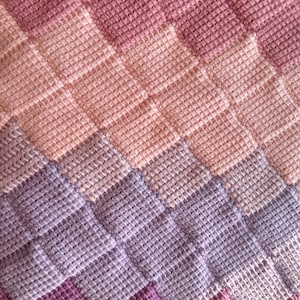 Puede incluir: Una manta de ganchillo con un patrón de chevron en tonos de rosa, morado y lavanda.