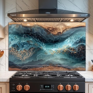 Op de afbeelding: Een decoratieve keukenachterwand met een abstract ontwerp. Het kunstwerk toont een mix van turquoise, blauwe en bruine tinten, met gouden accenten. Het ontwerp lijkt op een landschap met stromend water en organische vormen. De achterwand is geïnstalleerd boven een zwart gasfornuis.