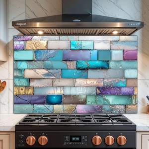 Op de afbeelding: Een kleurrijke keukenachterwand met een baksteenachtig ontwerp. Het ontwerp bevat een verscheidenheid aan kleuren, waaronder teal, blauw, paars, goud en grijs. De achterwand is geïnstalleerd achter een zwart fornuis en onder een roestvrijstalen afzuigkap.