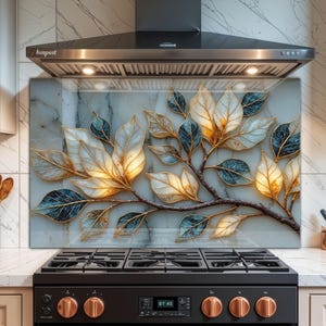 Può includere: Pannello decorativo per cucina con un ramo stilizzato e foglie. Le foglie sono bianche, dorate e blu, con bordi dorati. Lo sfondo ha un motivo simile al marmo. La cappa aspirante è in acciaio inossidabile.