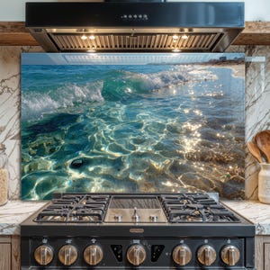 Könnte beinhalten: Eine Küchenrückwand aus Glas mit einer lebendigen Meereslandschaft. Das Bild zeigt klares türkisfarbenes Wasser mit Wellen, die sich an einem Sandstrand brechen. Sonnenlicht glitzert auf der Wasseroberfläche und erzeugt eine helle und einladende Atmosphäre.