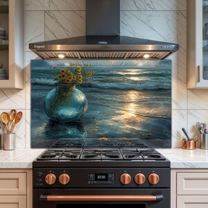 Può includere: Pannello paraschizzi da cucina in vetro raffigurante una serena scena oceanica con un vaso di girasoli. L'opera d'arte ha una tavolozza di colori blu e oro, con un riflesso dell'oceano sulla superficie. Il pannello è installato sopra un fornello nero.
