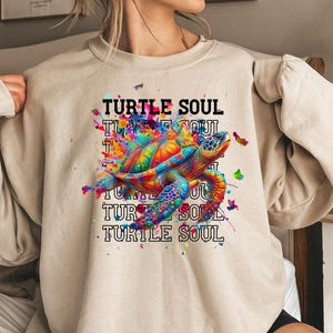 May include: A beige sweatshirt with a colorful graphic of a sea turtle and the text "TURTLE SOUL" repeated multiple times.