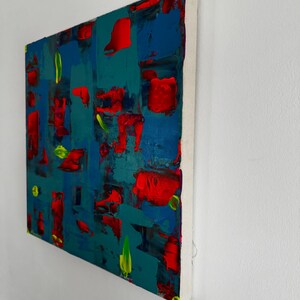 Puede incluir: Pintura abstracta acr&iacute;lica sobre lienzo con fondo turquesa, con trazos audaces de rojo, azul y verde. La obra est&aacute; montada sobre un bastidor blanco con bordes amarillos.