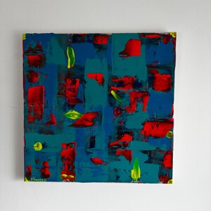 Puede incluir: Pintura abstracta de formato cuadrado. La obra presenta una superficie texturizada con pinceladas audaces en tonos azules, turquesa y rojo. Acentos amarillos y verdes a&ntilde;aden contraste. La firma del artista es visible en la esquina inferior izquierda.