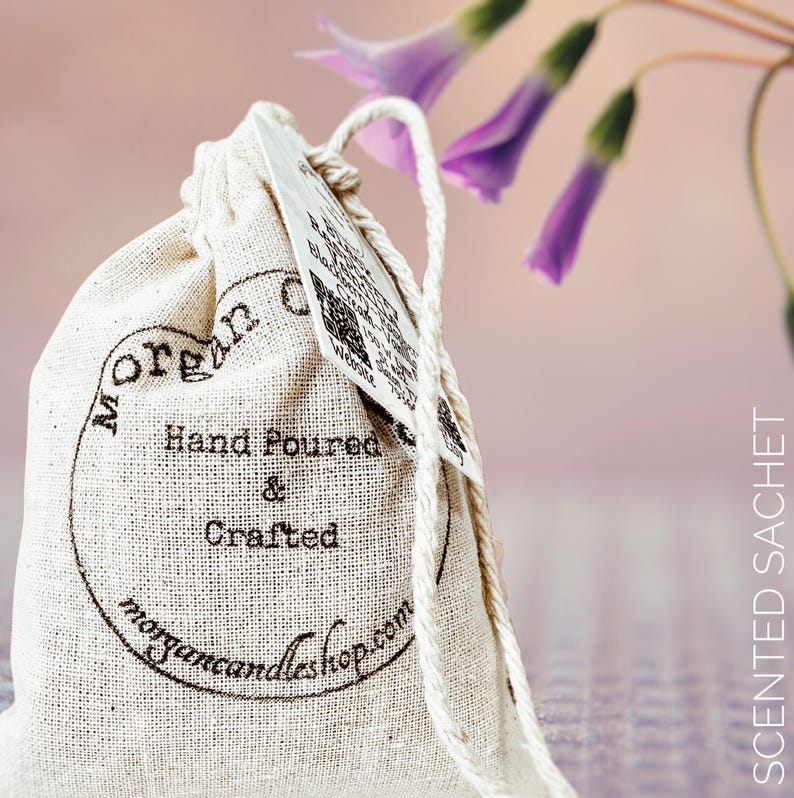 May include: A white cotton drawstring bag with a brown label that says "Morgan Candleshop.com" and "Hand Poured & Crafted". The bag is tied with a white string and is sitting on a purple and white patterned surface.