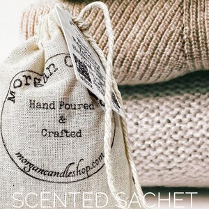 May include: A white linen sachet with black text that reads "Morgan Candleshop" and "Hand Poured & Crafted". The sachet is sitting on top of a beige knitted fabric.