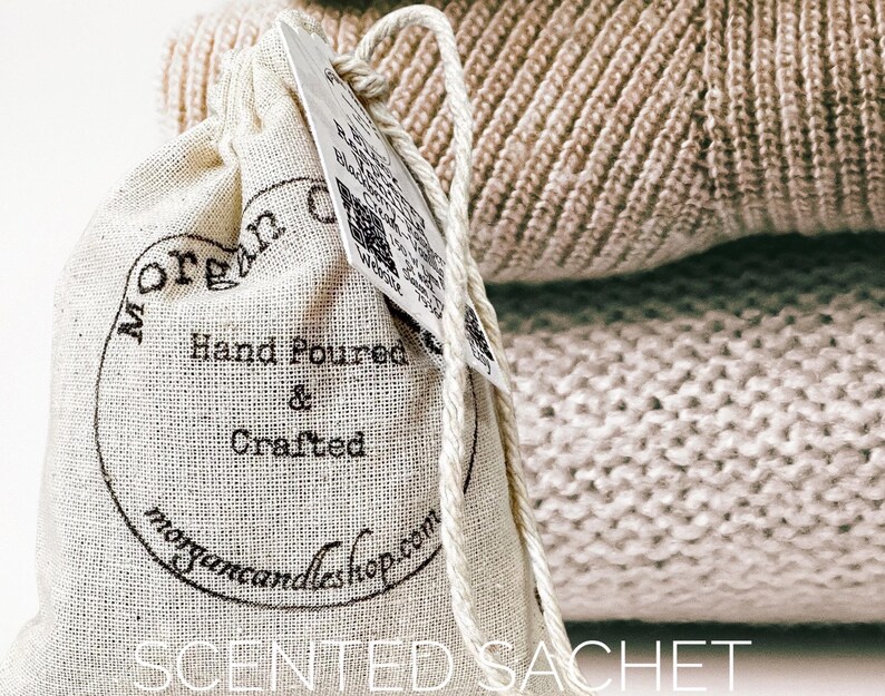 May include: A white linen sachet with black text that reads "Morgan Candleshop" and "Hand Poured & Crafted". The sachet is sitting on top of a beige knitted fabric.