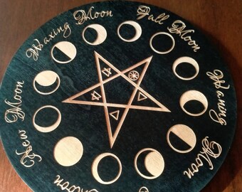 May include: A round wooden moon phase tracker with a dark green background. The tracker features a five-pointed star with a circle in the center and the words "Waxing Moon", "Full Moon", "Waning Moon", and "Dark Moon" around the edge.