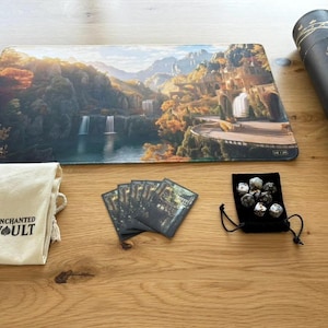 Może przedstawiać: Zestaw gier Enchanted Vault z matą z krajobrazem, kartami, kośćmi i tubą do przechowywania. Mata do gry przedstawia wodospad i widok na góry. W zestawie znajduje się również worek ze sznurkiem z logo Enchanted Vault.