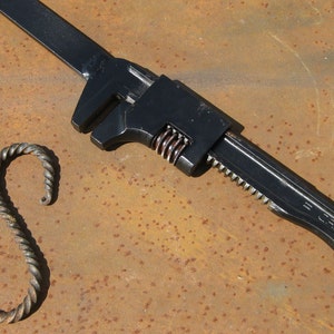May include: A black adjustable wrench with a serrated jaw and a spring-loaded handle. A twisted metal hook is in the foreground.