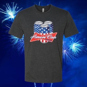 May include: Dark gray t-shirt featuring a graphic of three beverage cans with a red, white, and blue design. The cans are decorated with stars and stripes, and the text "Ameri Can" is displayed below them. The shirt has a crew neck.