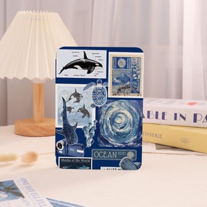 Op de afbeelding: Een donkerblauw decoratief item met een collage van afbeeldingen met oceaanthema, waaronder een diagram van een orka, een Japanse postzegel en een wervelend blauw ontwerp. De tekst "OCEAN BLVD" is zichtbaar.
