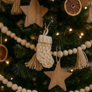 May include: A Christmas tree adorned with a variety of decorations. The tree displays wooden star ornaments, a crocheted stocking, dried orange slices, and a garland of wooden beads. The ornaments are in neutral tones, creating a rustic and festive holiday display.