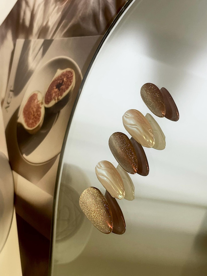 May include: A set of six oval-shaped nail polish colors. The colors are a light brown with gold glitter, a light brown with a swirl pattern, a light brown with gold glitter, a light brown with a swirl pattern, a light brown with gold glitter, and a light brown with a swirl pattern.