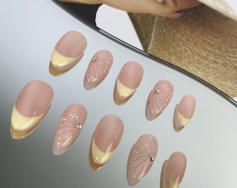 May include: Set of ten nude-colored press-on nails with a yellow accent on the tips and a 3D design on some nails.
