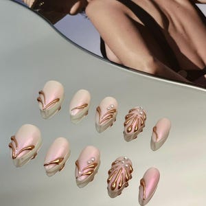 Könnte beinhalten: Set mit zehn pinkfarbenen und goldenen Press-on-Nägeln mit verschiedenen Designs, darunter Wirbel, Linien und abstrakte Formen.