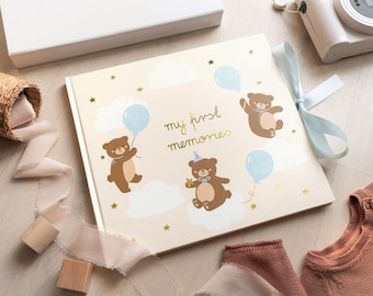 May include: A beige photo album with a gold inscription "my first memories" and illustrations of brown bears and blue balloons.